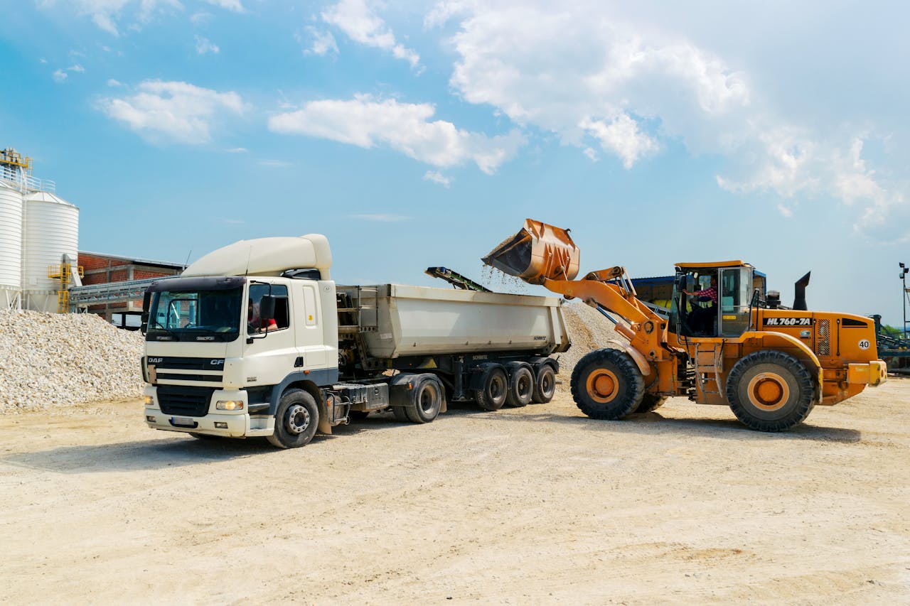 Services Excavator loading materials into a heavy-duty truck at a sunny construction site.
